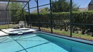 A swimming pool with a sunshade structure, a lounge chair, and a hedge in the background. - Gb1616 (Clermont)