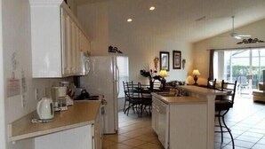 A kitchen with white cabinets, a coffee maker, and a dining area with a table and chairs. - Gb1616 (Clermont)