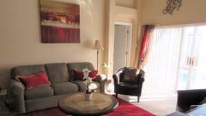 Una sala de estar con un sofá gris, un tapete rojo, un sillón negro y un cuadro en la pared.