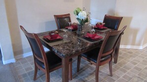 Una mesa de comedor con cuatro sillas, un florero y servilletas rojas.