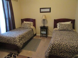 A hotel room with two beds, each with zebra-patterned bedding, a small bedside table with a lamp, and a framed inspirational quote on the wall.