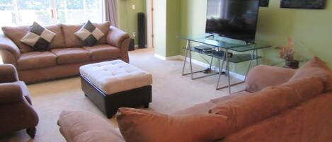 A living room with a brown sofa, a glass coffee table, and a television on a stand.