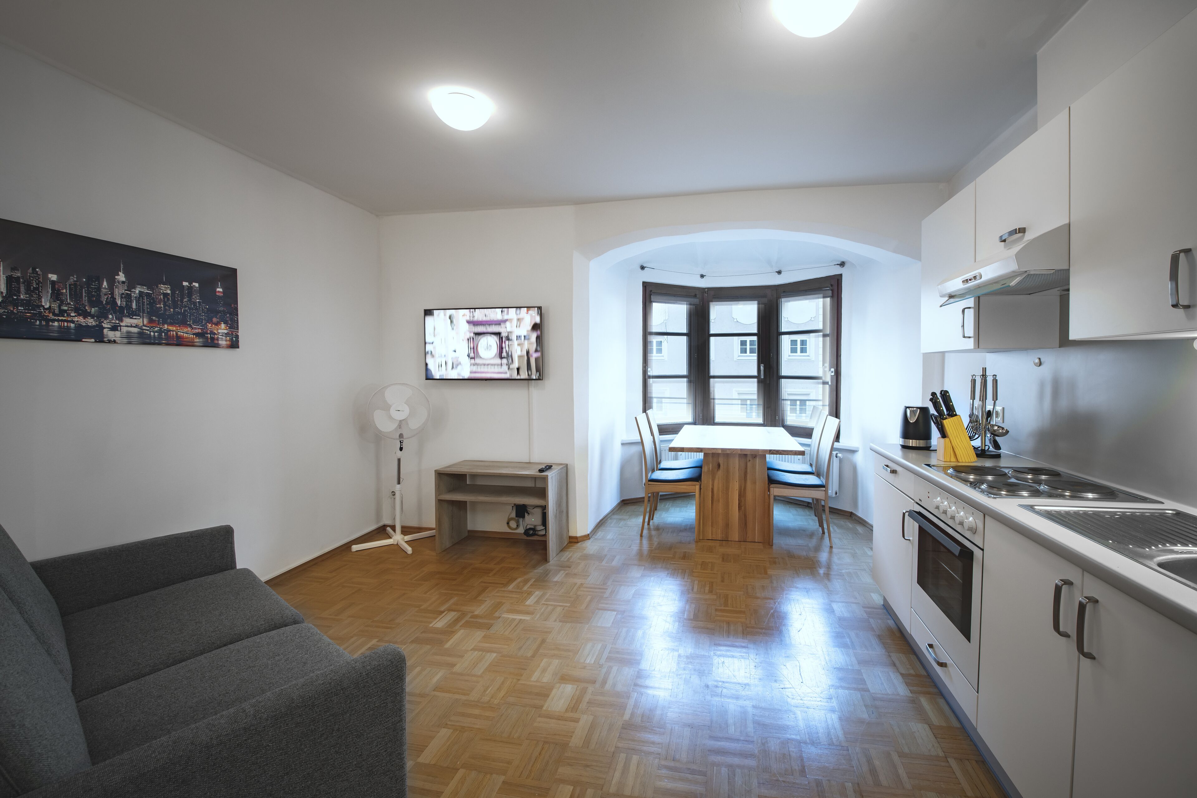 Une cuisine moderne avec un coin repas, un plancher en bois et un tableau représentant un paysage urbain.