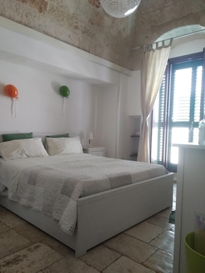 A bedroom with a bed, a nightstand, a lamp, and a window with curtains. - Dimora Dioniso (Polignano a Mare)