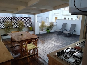 An outdoor patio with a wooden table and chairs, a gas stove, and potted plants. - Dimora Dioniso (Polignano a Mare)