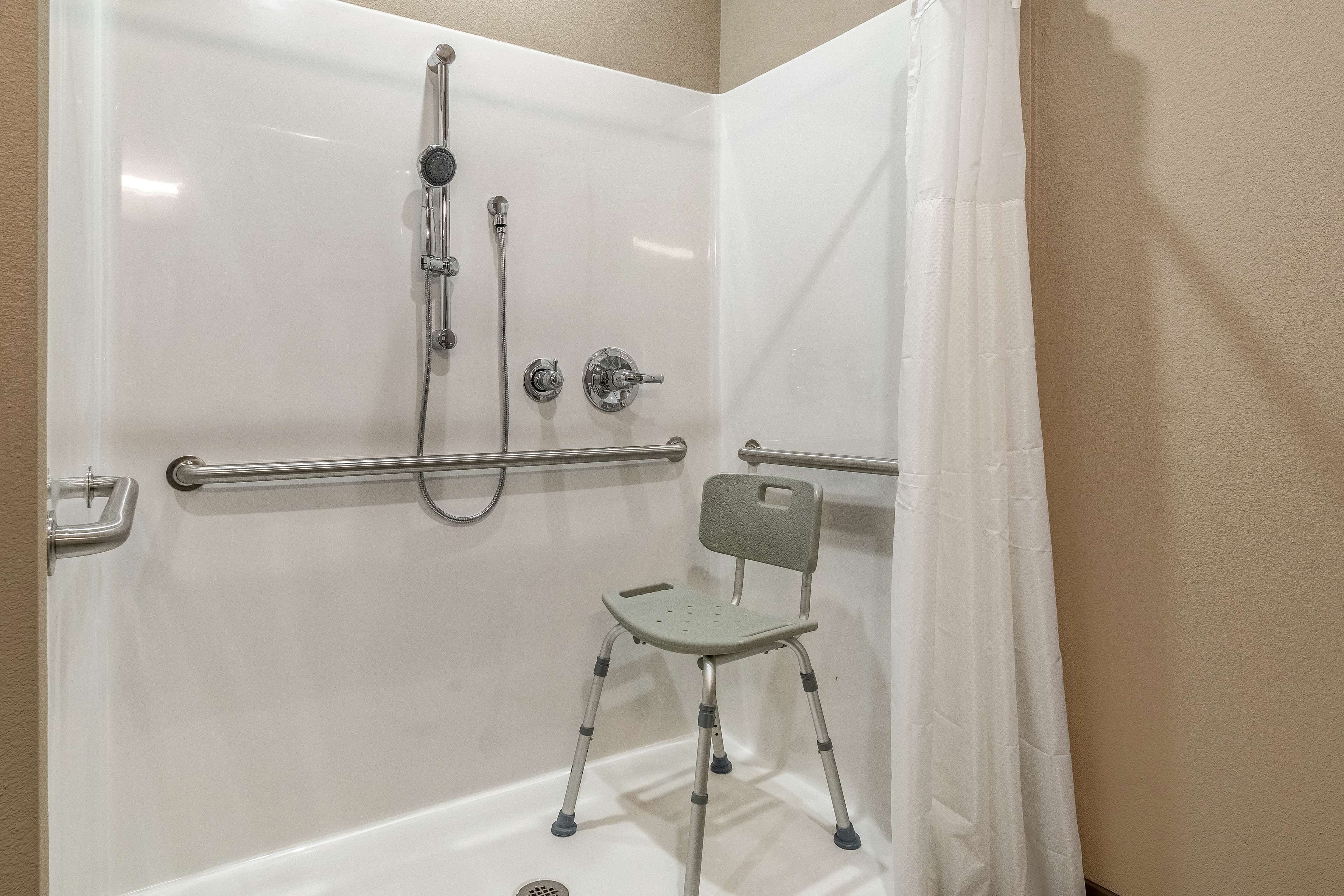 A shower area with a grab bar, a showerhead, and a chair.