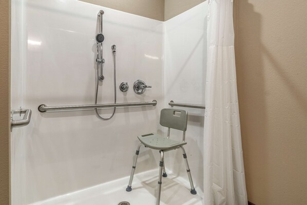 A shower area with a grab bar, a showerhead, and a chair.