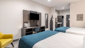 Une chambre d’hôtel avec deux lits, un bureau avec un ordinateur, une chaise, une télévision et un miroir.