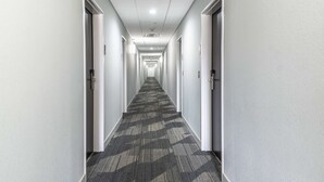 Un long couloir étroit, typique d’un hôtel, avec des murs blancs et un sol recouvert de moquette.