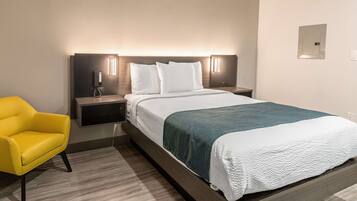 Une chambre d’hôtel avec un grand lit, une table de chevet avec un téléphone et une lampe, une chaise jaune et un luminaire fixé au mur.