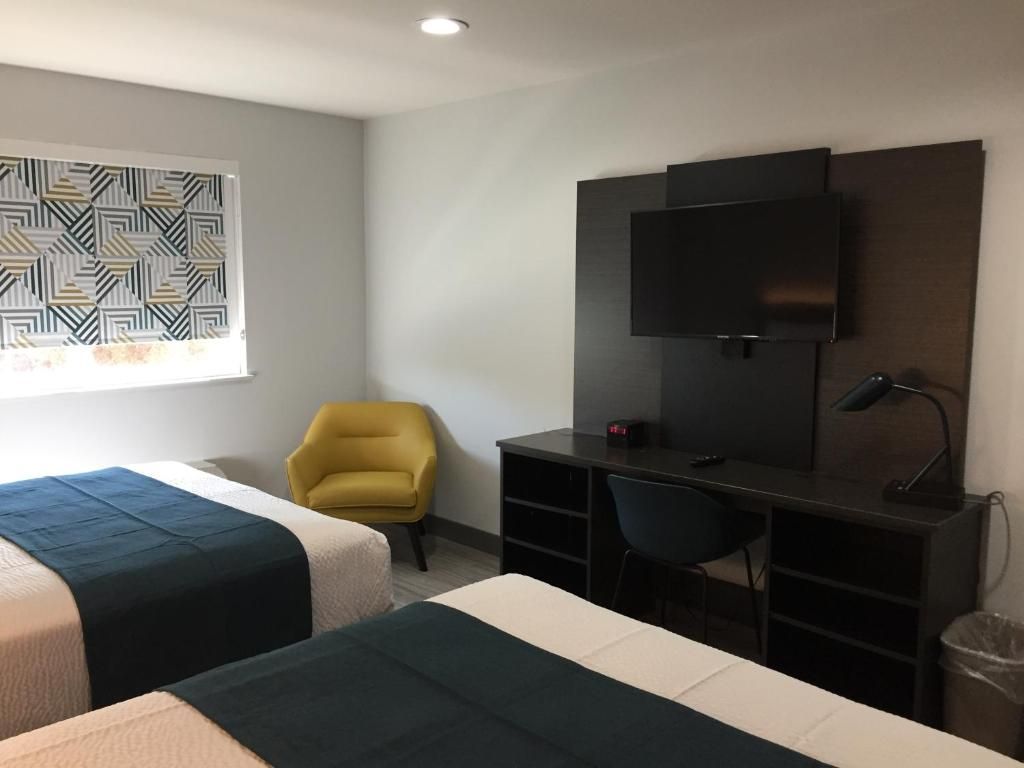Habitación de hotel con dos camas, un escritorio, una silla, un televisor y una persiana con diseño.