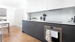 A modern kitchen with white cabinets, a stainless steel oven, and a wooden floor.