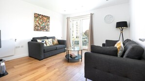 A modern living room with two grey sofas, a glass coffee table, and a large window with curtains.