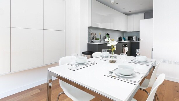 A modern kitchen with white cabinets, a dining table set for four, and a small island with a vase of flowers.