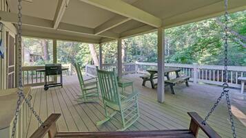 A covered porch with wooden flooring, rocking chairs, picnic tables, and a swing.