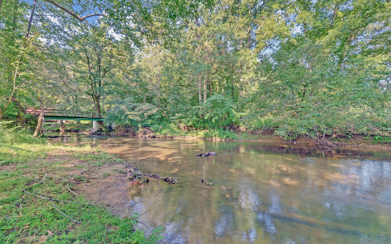 Une scène paisible au bord de la rivière, avec un pont, une végétation luxuriante et une eau calme.