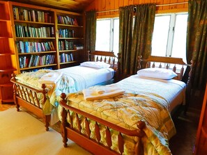 Une chambre à coucher avec deux lits en bois, une bibliothèque et une fenêtre avec des rideaux.