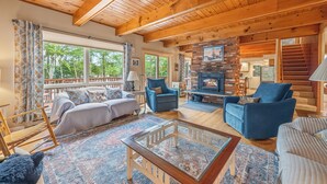 A spacious living room with a wooden ceiling, a fireplace, and large windows offering a view of the outdoors. - Riesses Peace - Beautiful 4 bedroom, 3 bath home on Cupsuptic Lake (Oquossoc)