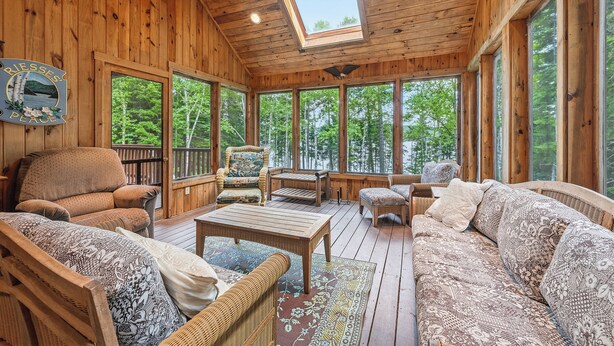 A wooden cabin with a large skylight, wicker furniture, and a view of the forest. - Riesses Peace - Beautiful 4 bedroom, 3 bath home on Cupsuptic Lake (Oquossoc)