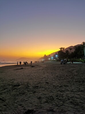 A beach at sunset with people walking and a vehicle parked on the sand. - Pousada Irashai (São Sebastião)