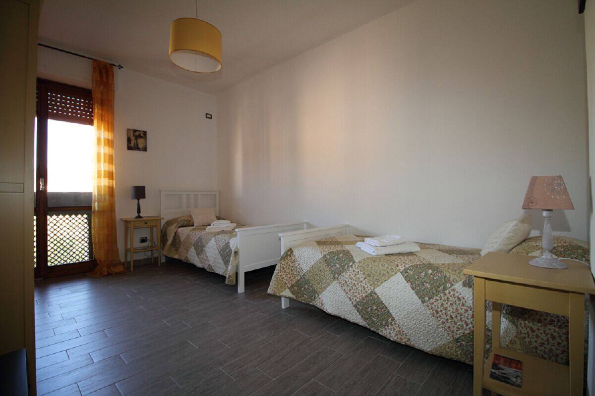 Una habitación con dos camas, una mesita, una lámpara y un ventanal con cortinas.