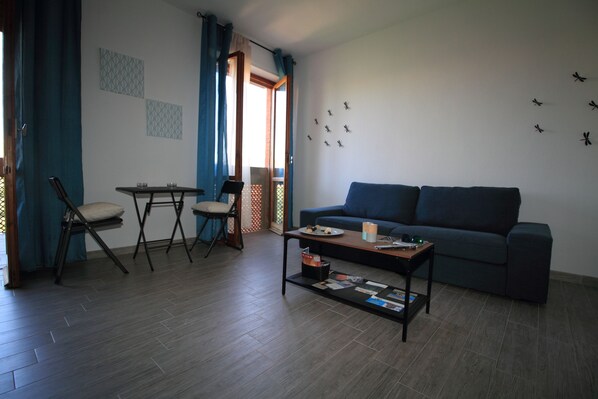 A living room with a sofa, a coffee table, and a dining area with a table and chairs. - B&B Libellula (Iglesias)
