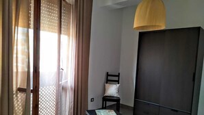 A room with a sliding glass door, a chair, a small table, and a wardrobe. - B&B Libellula (Iglesias)