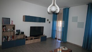 A modern living room with a flat-screen TV, wooden entertainment unit, and a coffee table. - B&B Libellula (Iglesias)