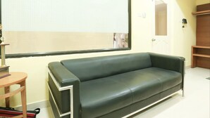 Una habitación con un sofá de cuero negro, una pequeña mesa de madera y un ventanal con diseño de cuadrícula.
