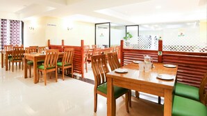 Un restaurante con mesas de madera y sillas acolchadas verdes, un suelo con estampado de cuadros y un cartel de 'No Fumar' en la pared.