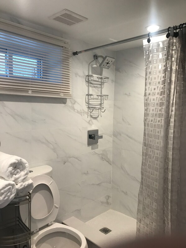 A bathroom with a toilet, a shower, and a towel rack. - We have beautiful, serene environment for your comfort. (Queens)