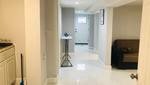 Un couloir avec un sol blanc, un lampadaire, une porte au fond et un canapé à l’arrière-plan.