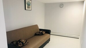 Un salon moderne avec un canapé marron, deux coussins à motifs, une plante décorative dans un cadre et une horloge murale.