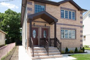 A two-story brick building with a covered front porch, two front doors, and a small set of stairs leading up to the entrance. - We have beautiful, serene environment for your comfort. (Queens)