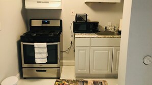 Une cuisine de taille réduite avec des meubles blancs, une cuisinière en acier inoxydable, un four à micro-ondes et un évier.