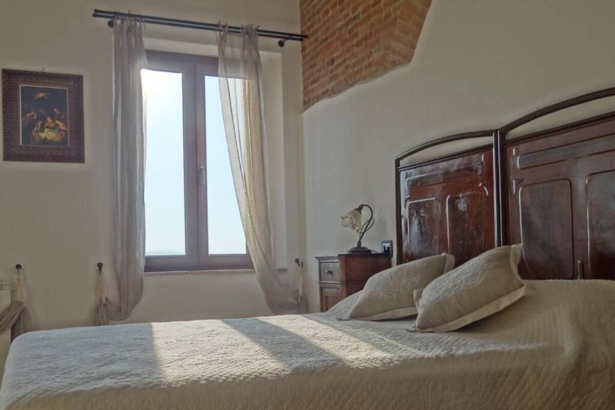 Ein Schlafzimmer mit einem Bett, einem Fenster mit Vorhängen, einem Holzkopfstück und einem kleinen Nachttisch mit Lampe.