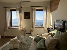 Un dormitorio con cama, almohadas, una mesita de noche y una ventana con cortinas.