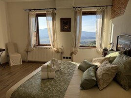 A bedroom with a bed, a chair, a window with curtains, and a view of the landscape.