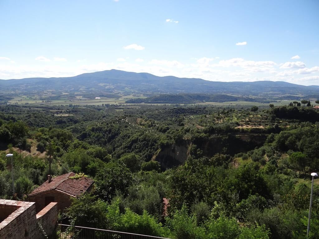 Paisaje rural con vistas a montañas distantes, un pequeño edificio con techo de tejas y vegetación exuberante.