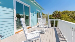 Een blauw huis met een witte veranda, witte stoelen en een witte balustrade.