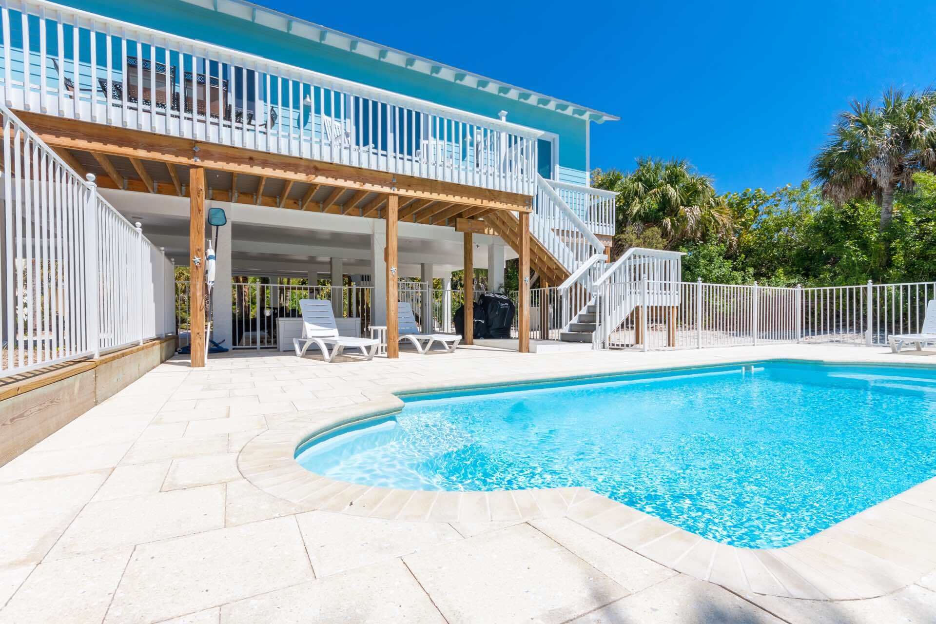 A pool area with a covered deck, lounge chairs, and a staircase leading to a balcony.