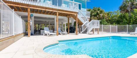 A pool area with a covered deck, lounge chairs, and a staircase leading to a balcony.