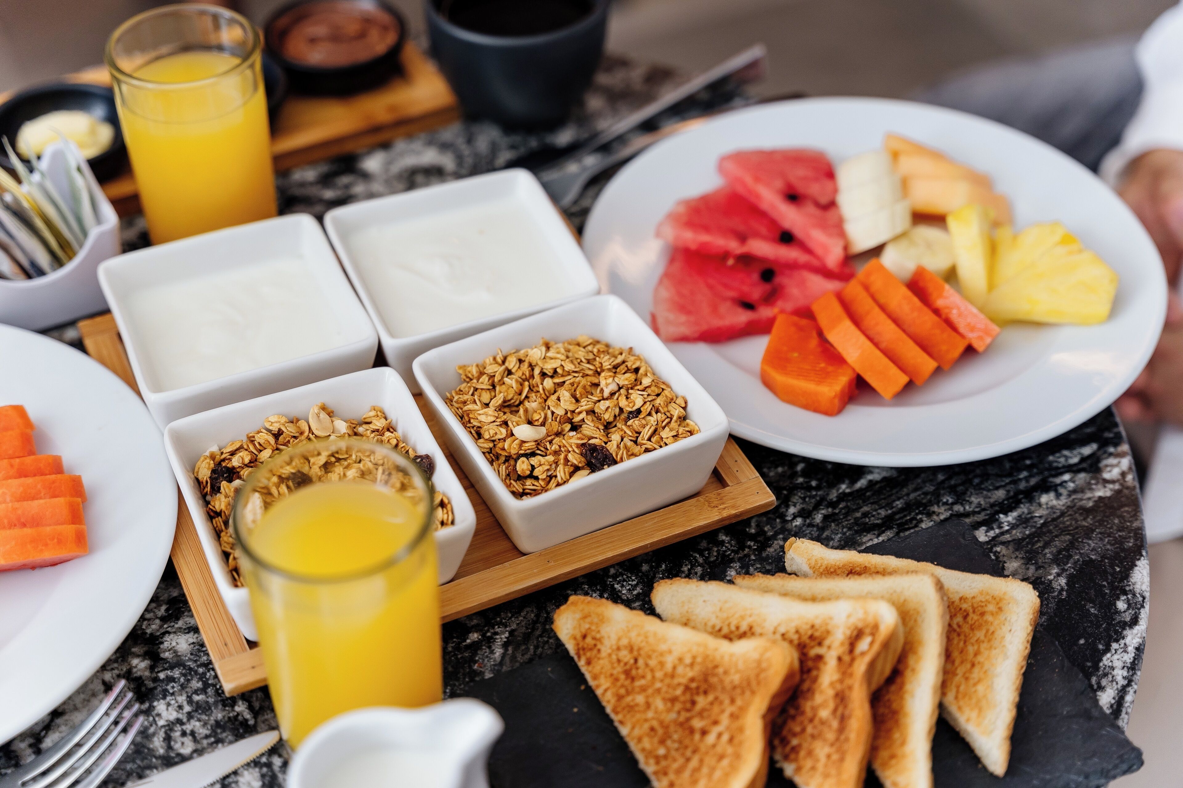 A breakfast tray with toast, fruit, yogurt, granola, and orange juice.