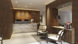 Un moderno mostrador de recepción de hotel con un diseño de paneles de madera, un mostrador de mármol y una zona de estar con lámpara y libros.