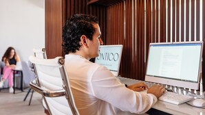 Una persona usando una computadora de escritorio en una habitación con paneles de madera y una silla blanca.
