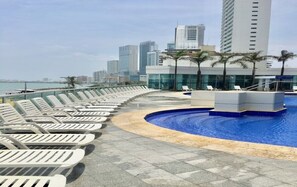 Un espace piscine aménagé sur le toit, avec des chaises longues et une vue sur le panorama urbain.
