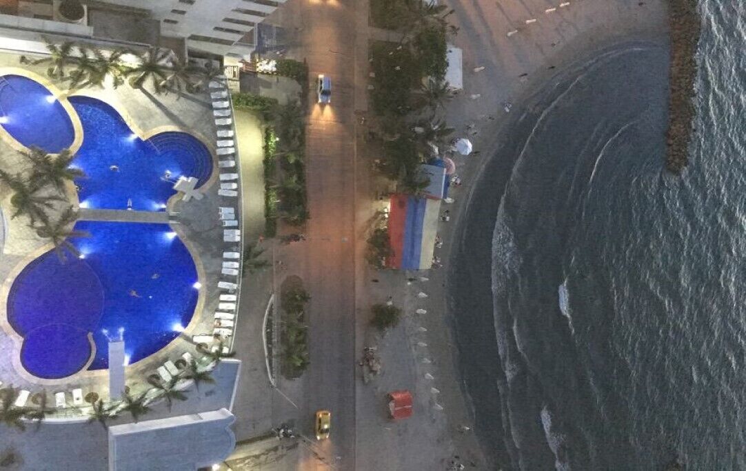 Ein Hotel an der Küste mit Poolbereich, einer Straße direkt am Strand und Blick auf den Ozean.