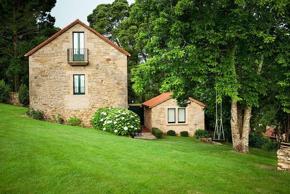 A stone house with a balcony, a smaller attached building, and a well-maintained lawn.
