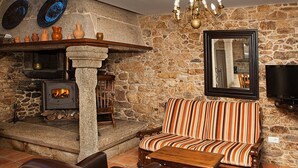 A stone-walled room with a fireplace, a striped sofa, and a television. - Stone house restored in the middle of nature (Lage - A Coruña)