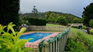 A swimming pool surrounded by a wooden fence, with a grassy area and trees in the background. - Stone house restored in the middle of nature (Lage - A Coruña)